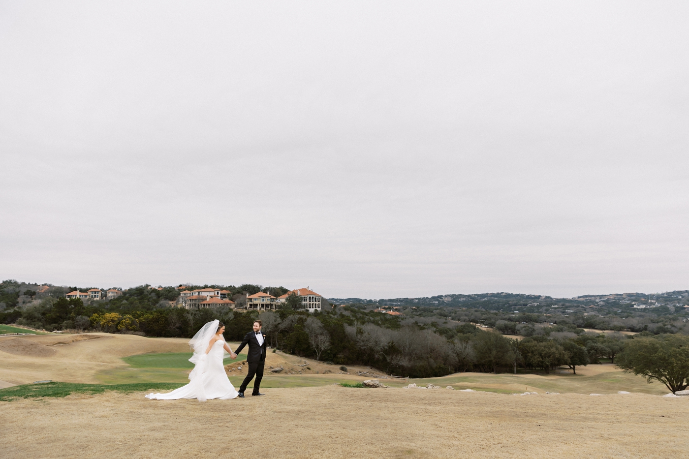 Couple holding hands on the lawn of Omni Barton Creek, overlooking the hills
