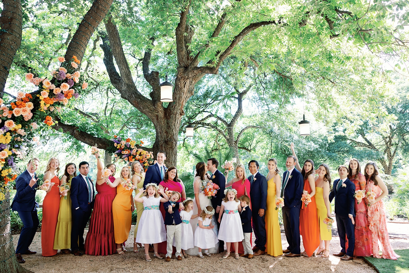 Colorful bridal party in navy blue suits and pink, orange, and yellow gowns