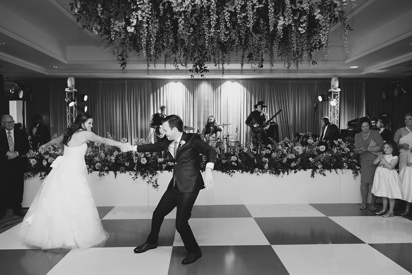 Bride and groom dancing on a checkered dance floor with hanging flowers