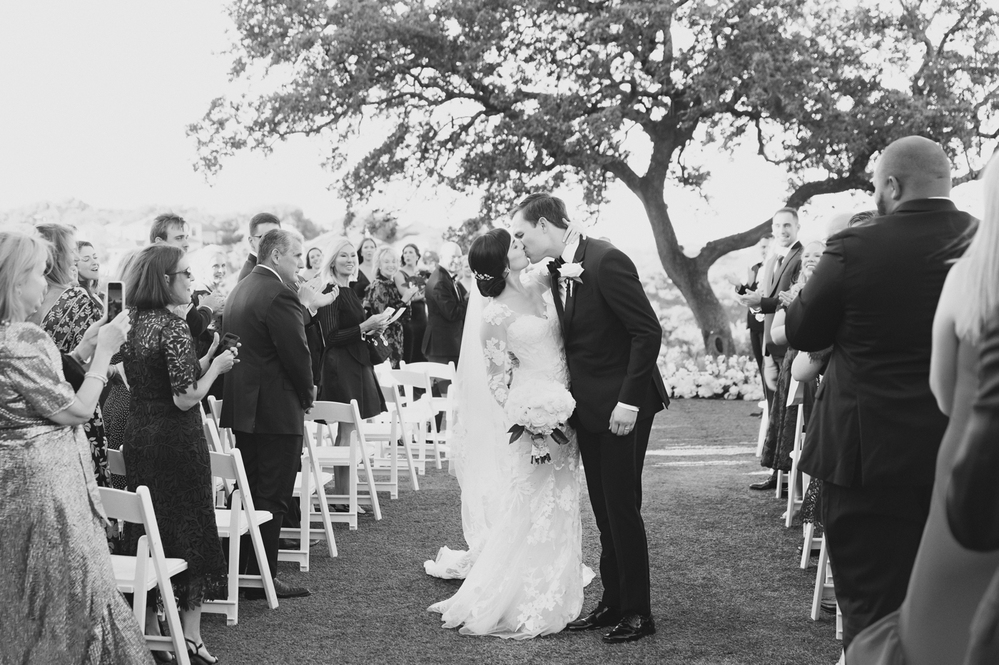 Black and white image of a bride and groom kissing at their wedding ceremony