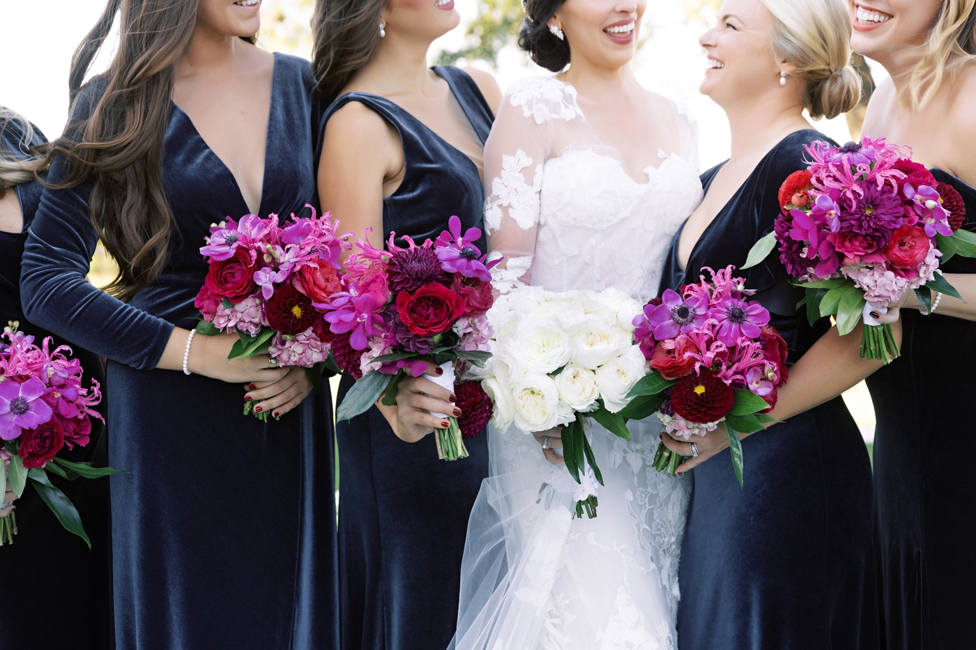 Blue velvet bridesmaids dresses, holding bright pink, red and fuchsia bouquets