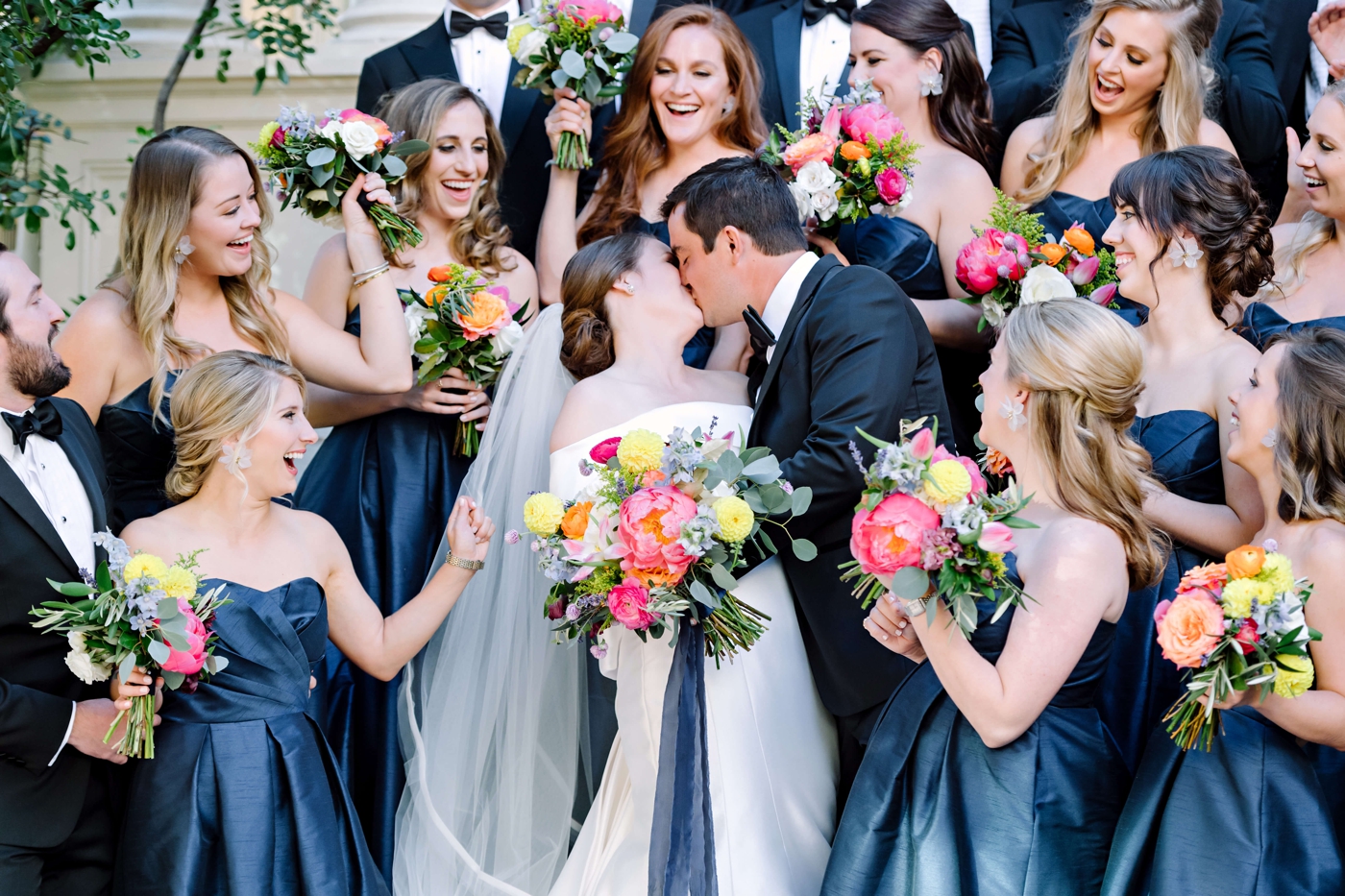 Bridesmaids in navy blue satin dresses, holding colorful bridal bouquets