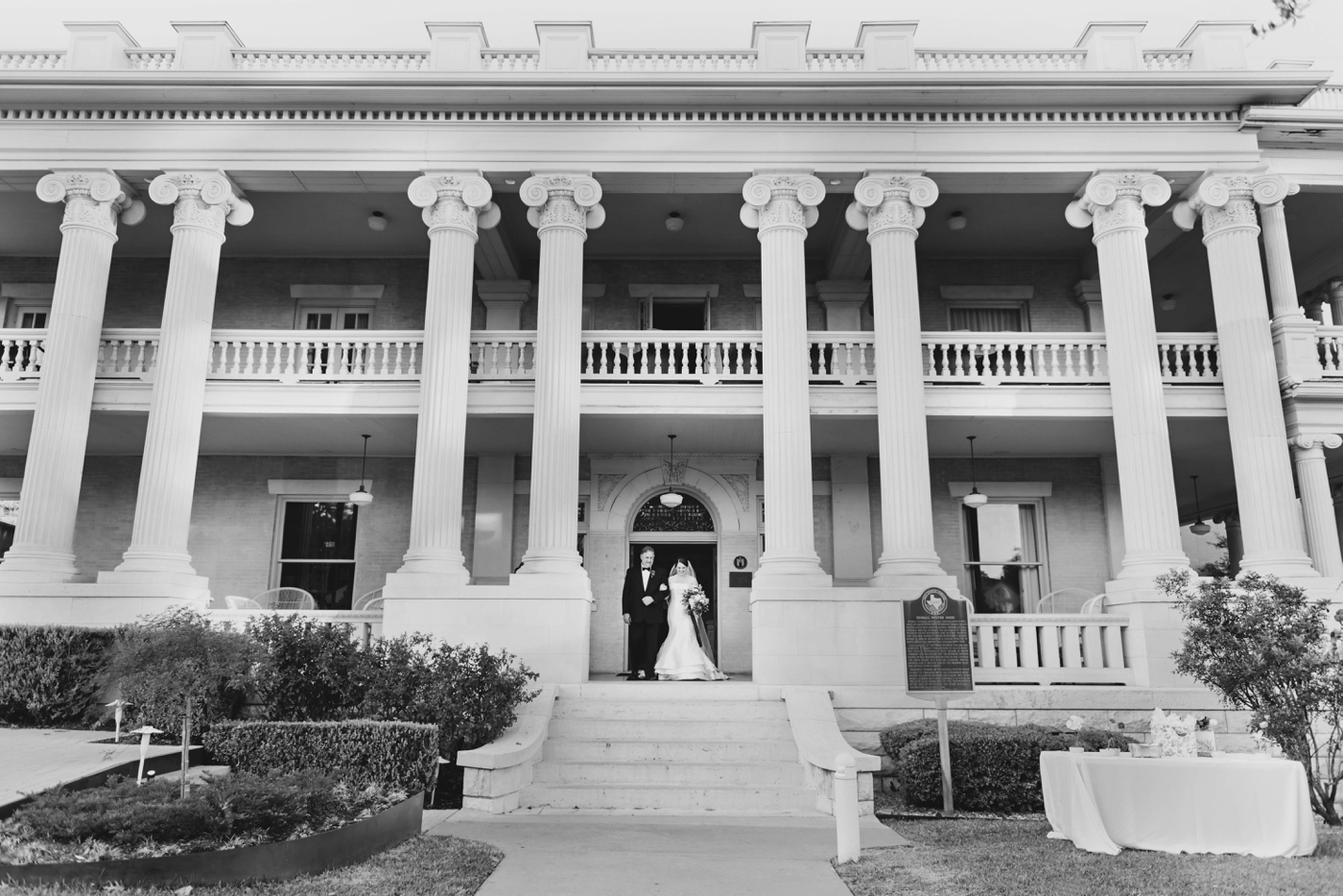 Black and white image of the front of Hotel Ella , with the bride walking down the stairs with her father