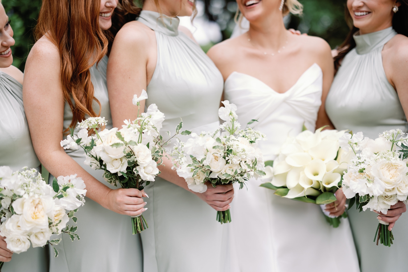 Bridesmaids in soft green satin dresses, holding all white bridal bouquets