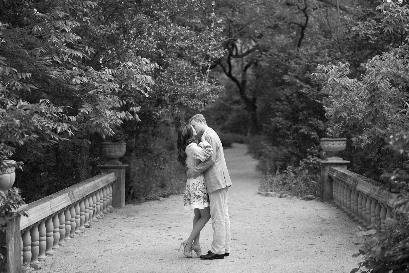 Black and white image of a couple at Laguna Gloria in Austin, on a bridge with a garden behind them